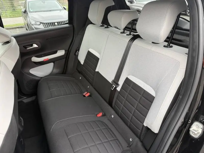 Vue intérieure côté arrière droit montrant les sièges bicolores gris clair et noir de la Citroën C3 électrique 2025.