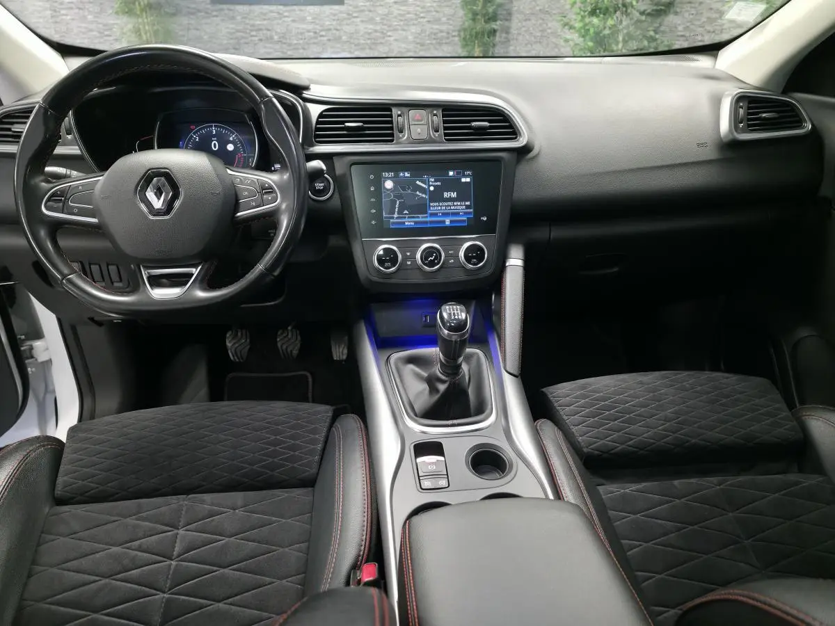 Vue intérieure avant du Renault Kadjar blanc 2020, volant cuir, console centrale avec écran tactile et levier de vitesses manuel.