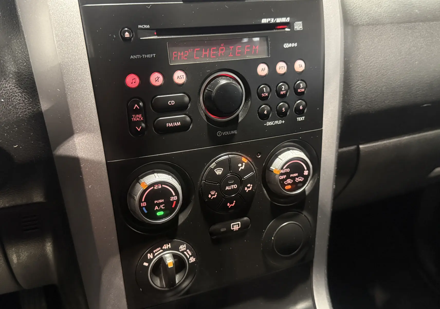 Vue rapprochée de la console centrale noire du Suzuki Grand Vitara gris 2007, avec commandes clim et radio affichant CHERIE FM.