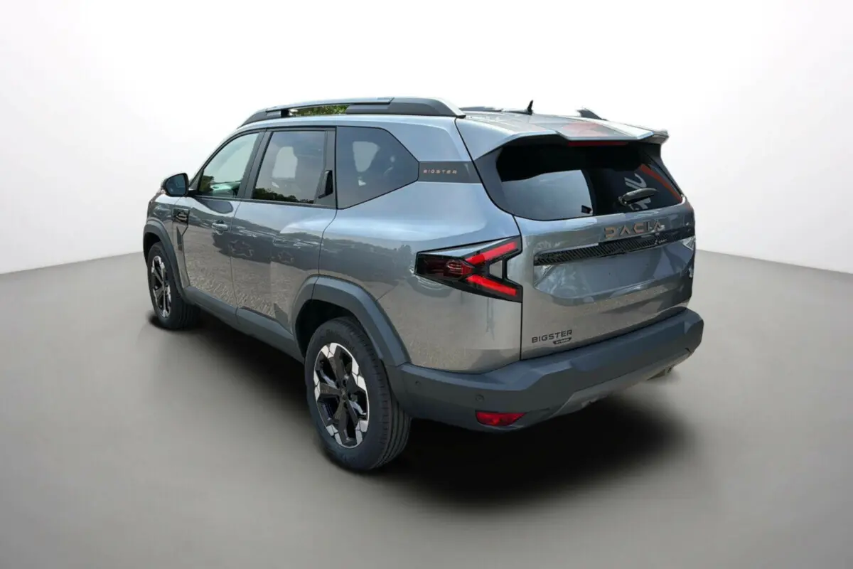 Vue 3/4 arrière droite du Dacia Bigster 2025 gris schiste, avec logo et feux arrière en forme de flèche rouge.