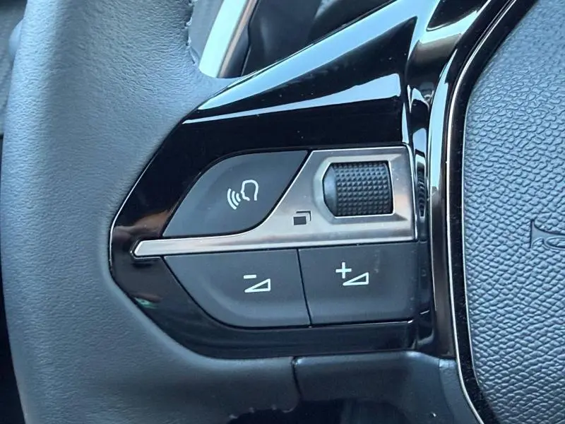 Gros plan sur les commandes vocales et volume au volant du Peugeot 2008 hybride bleu Obsession 2025.