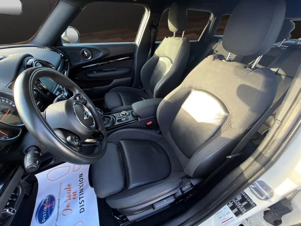 Intérieur avant droit d’une MINI Clubman blanc, sièges en cuir noir et tableau de bord avec écran tactile.
