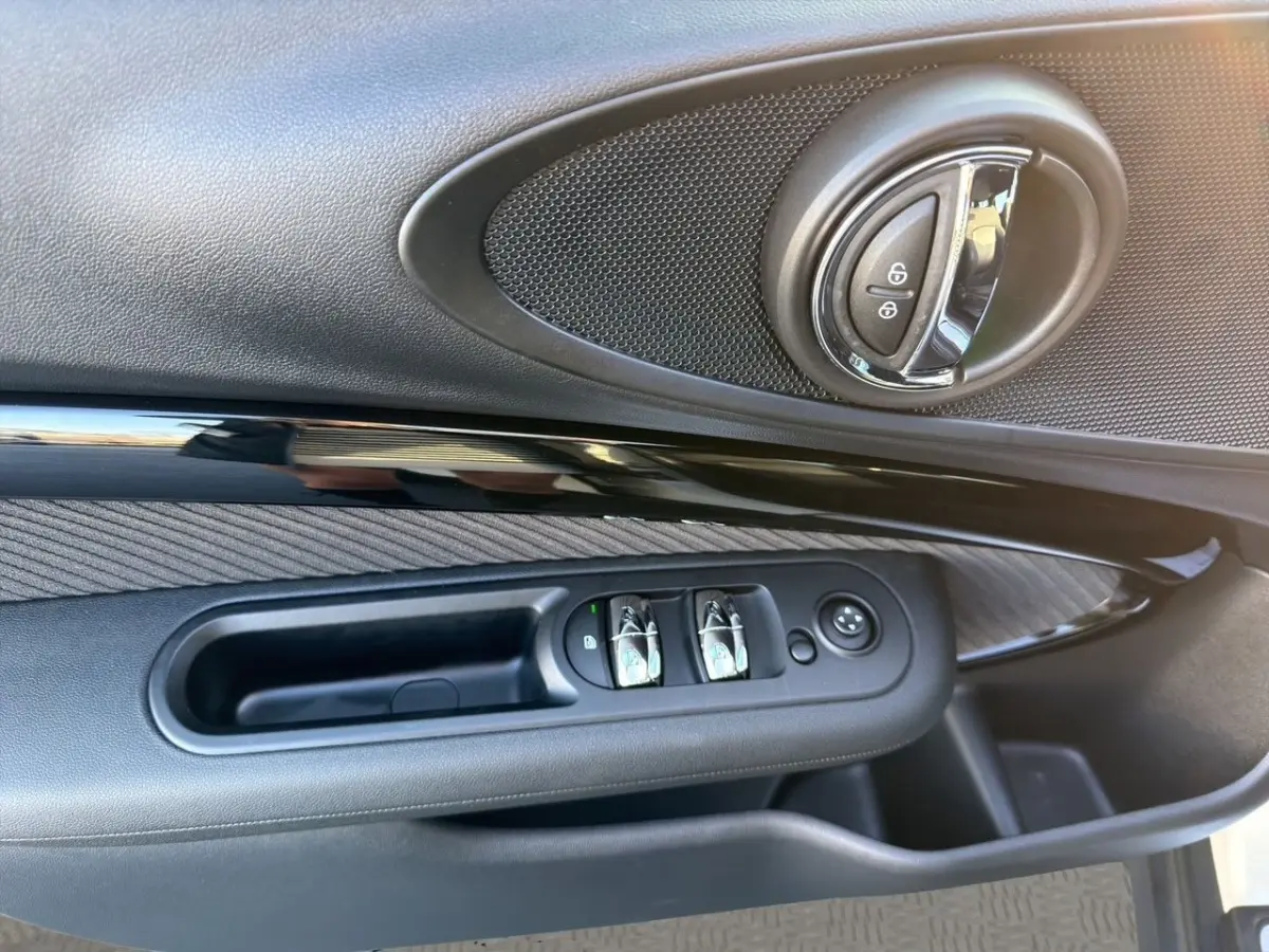 Gros plan sur la porte côté conducteur de la MINI Clubman blanche, montrant les commandes de vitres et la poignée intérieure ronde.