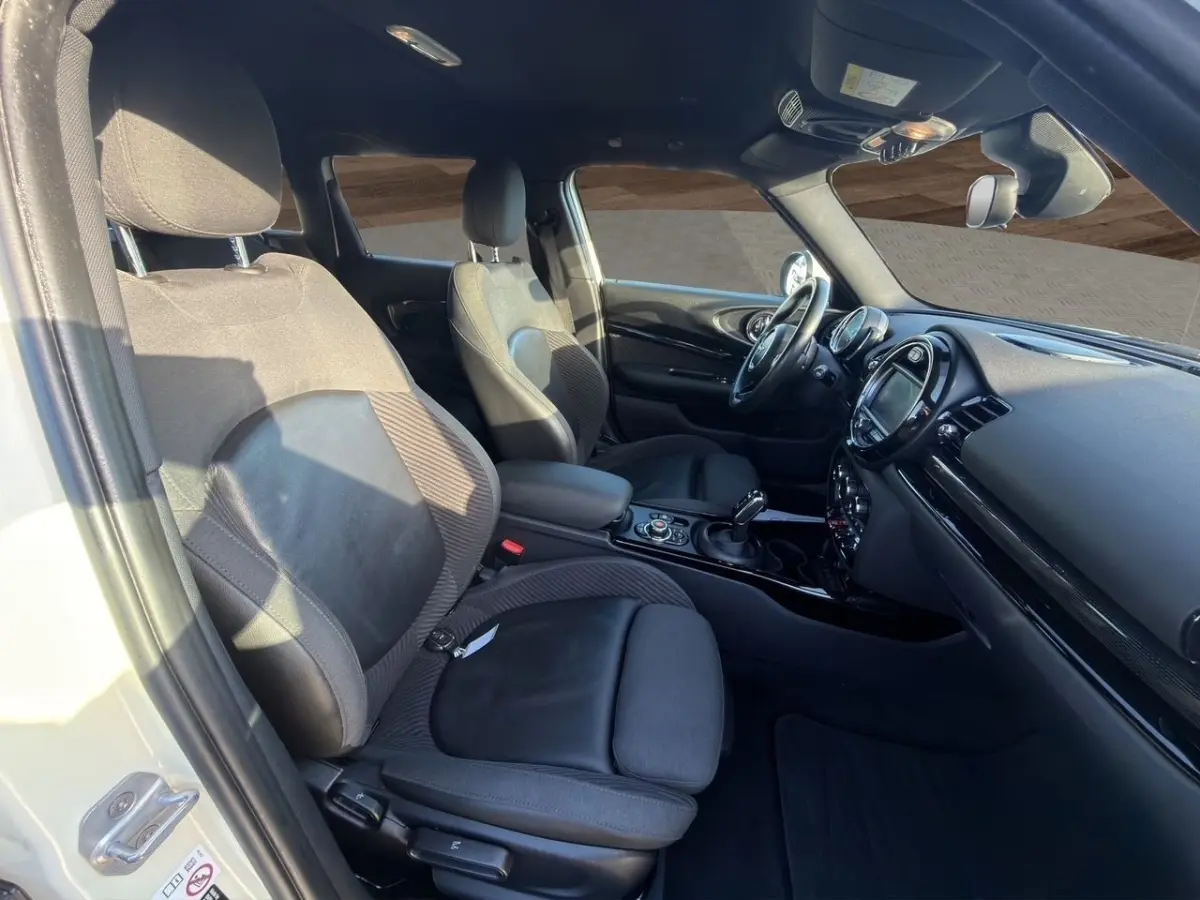 Vue intérieure côté conducteur de la MINI Clubman blanche, montrant sièges noirs et tableau de bord moderne avec écran tactile.