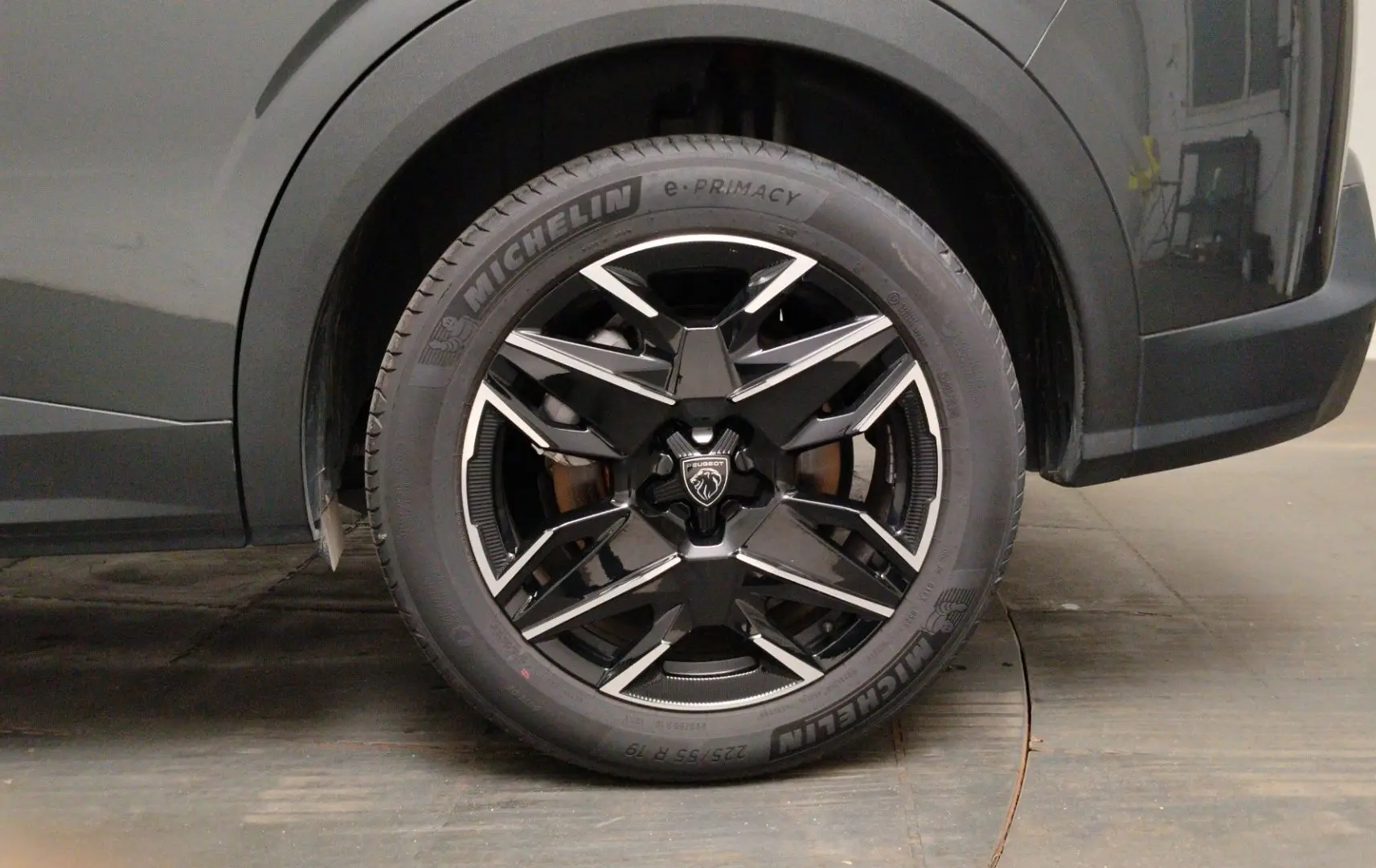 Gros plan sur la roue avant droite du Peugeot 5008 gris titane, jante noire à design géométrique brillant.