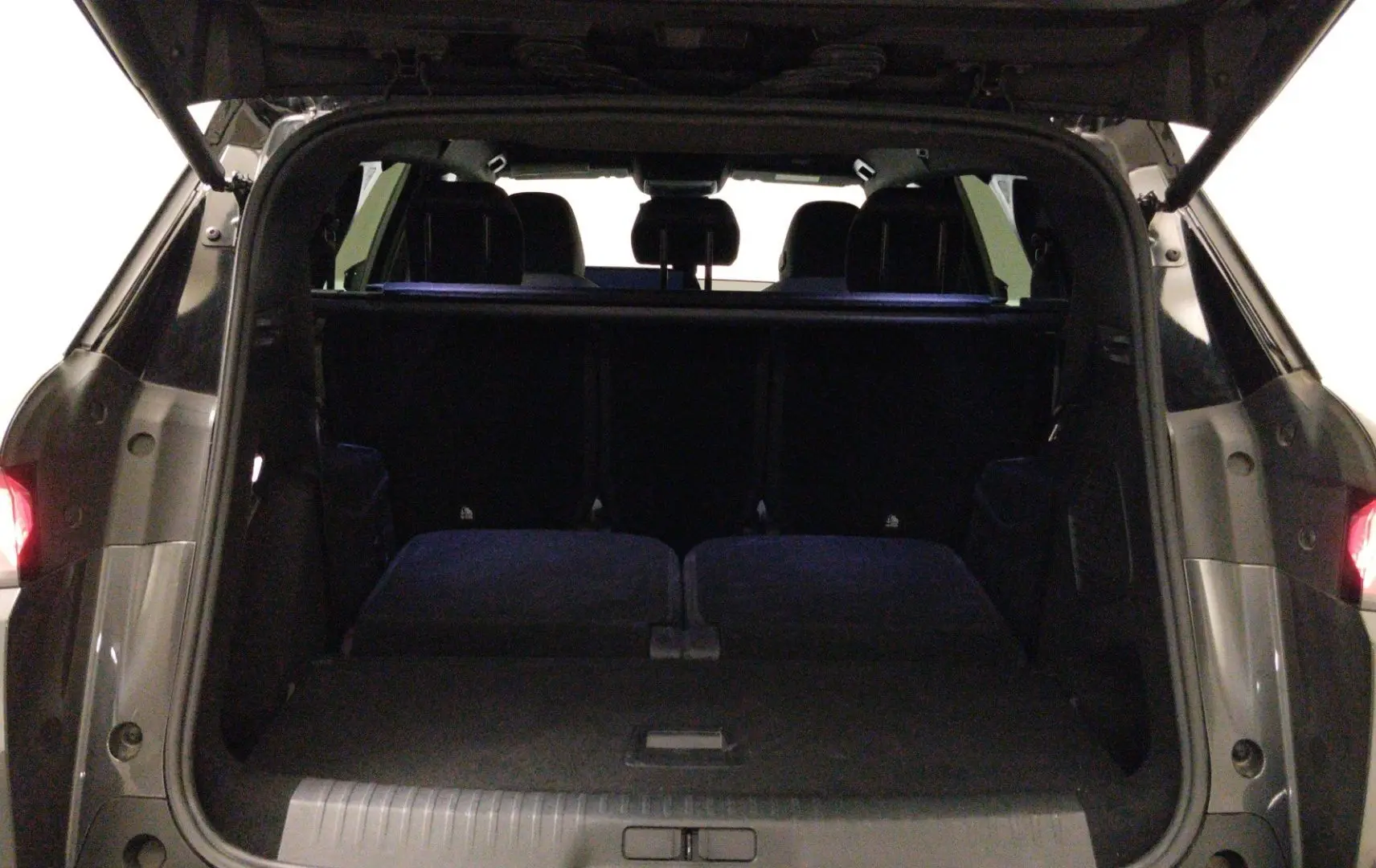 Coffre ouvert vu de l'arrière du Peugeot 5008 gris titane, montrant l'espace de chargement et les sièges arrière rabattus.