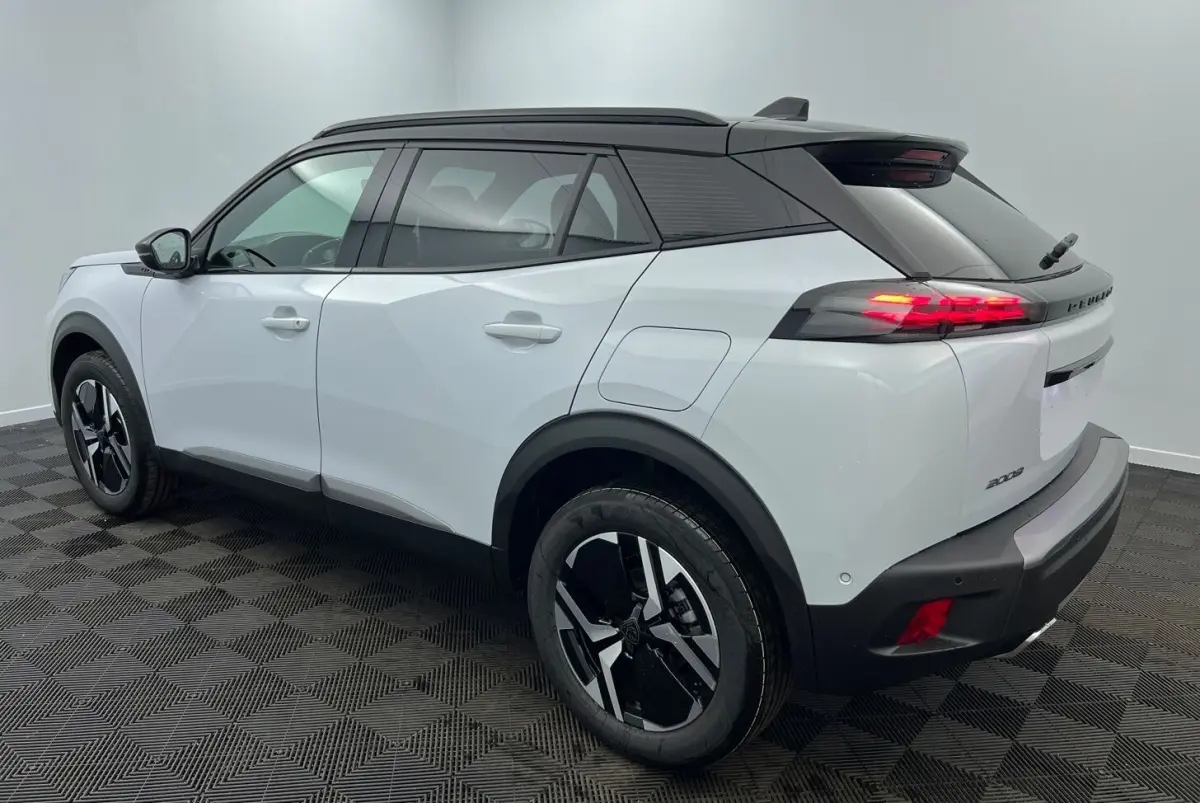 Vue 3/4 arrière droite du Peugeot 2008 Hybrid 145 GT blanc avec toit noir et feux arrière allumés.