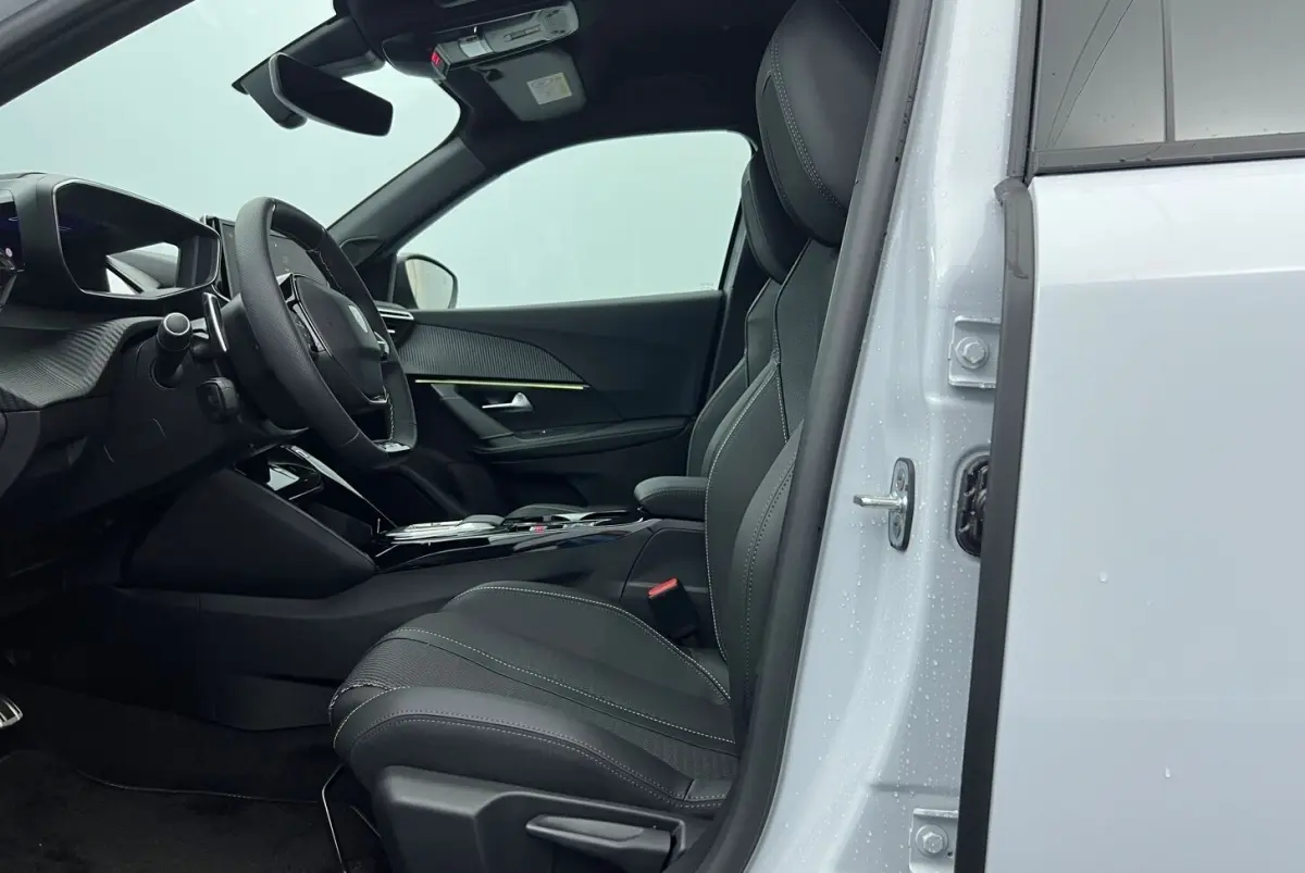 Vue intérieure côté conducteur du Peugeot 2008 Hybrid blanc, mettant en valeur le siège et le volant cuir multifonctions.