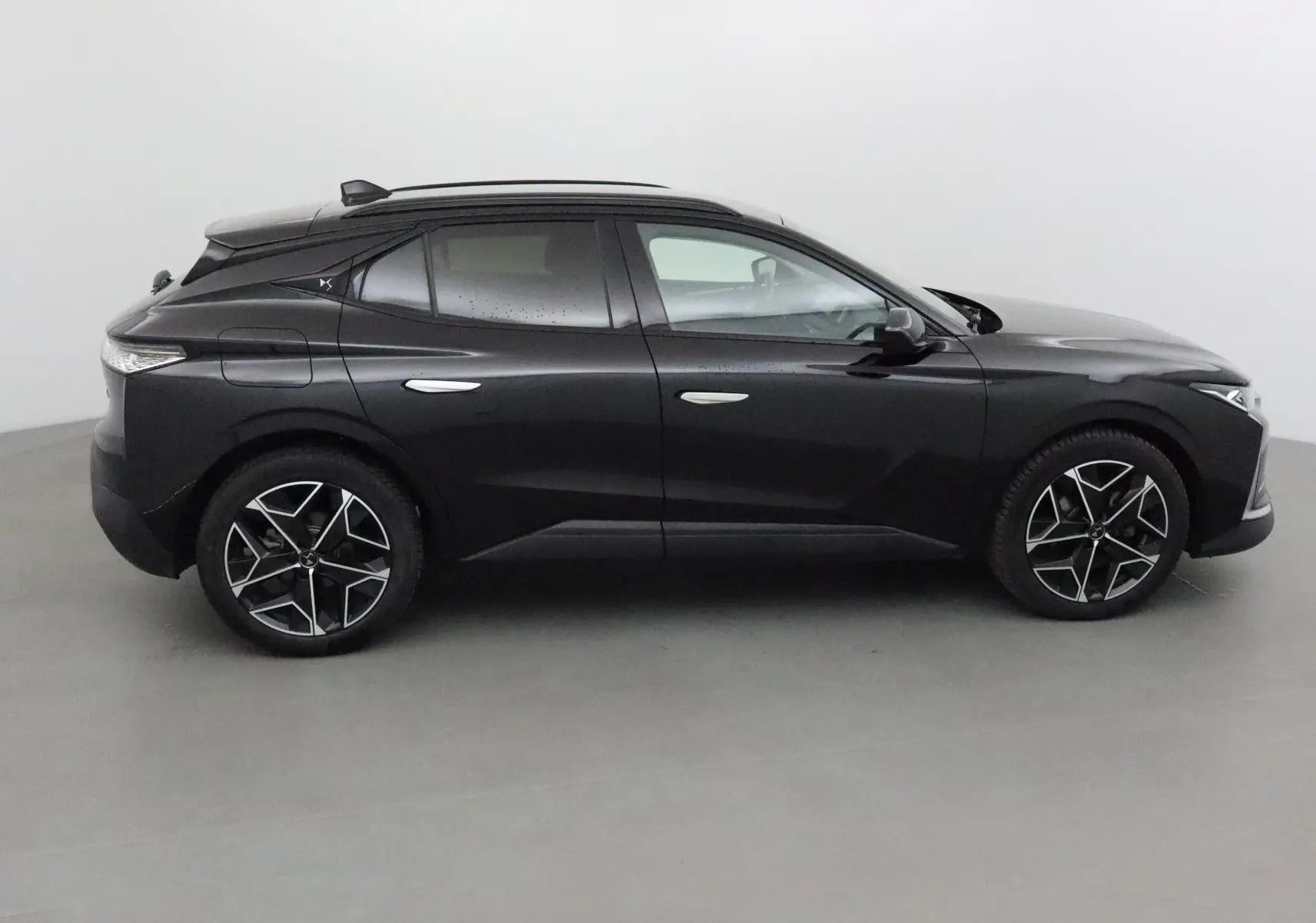 Profil côté gauche d'une DS4 noire 2022 avec jantes alliage noires et toit panoramique, dans un studio lumineux.