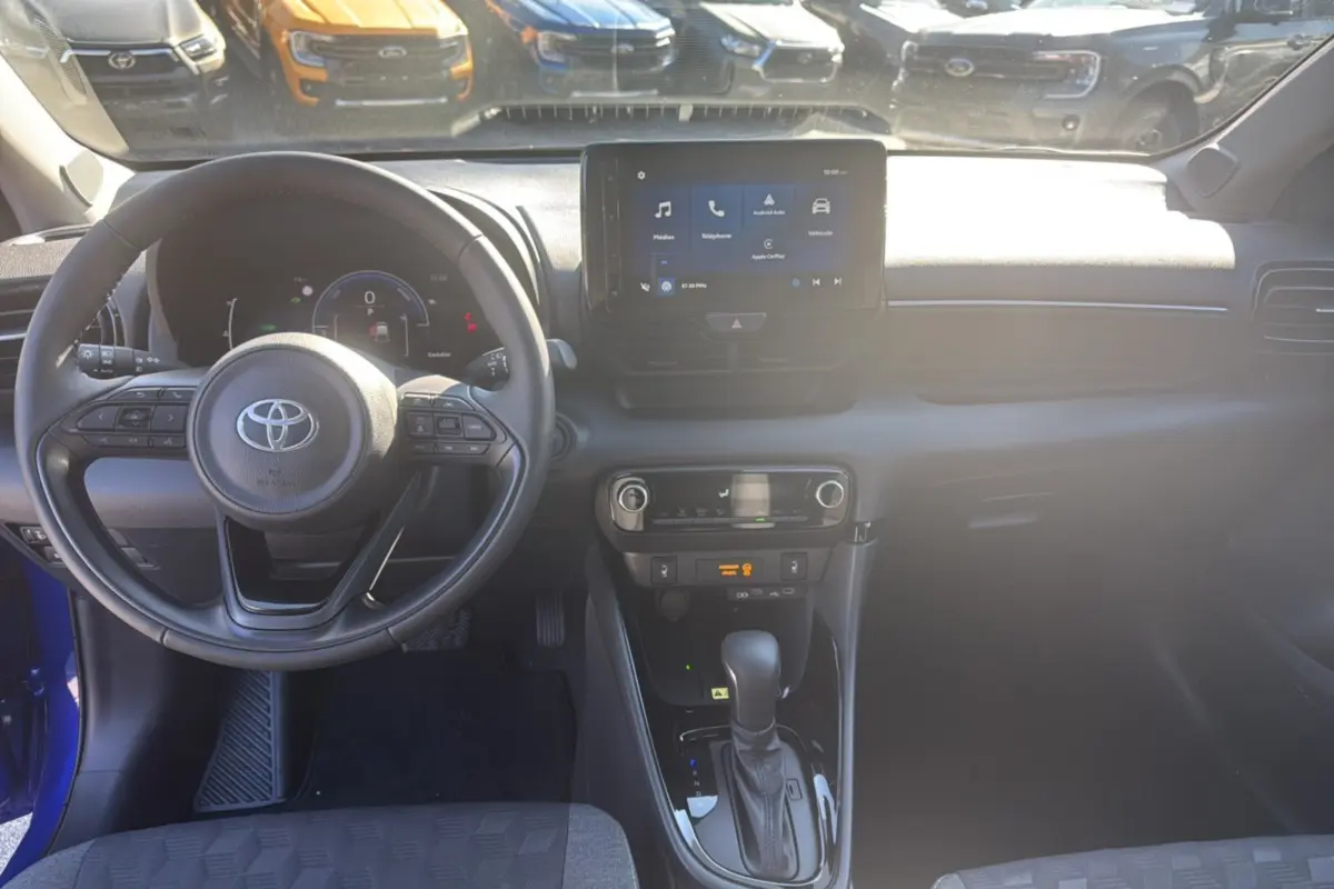 Intérieur de la Toyota Yaris 1.5 Hybrid 2025, vue du poste de conduite avec volant multifonction et écran tactile central.