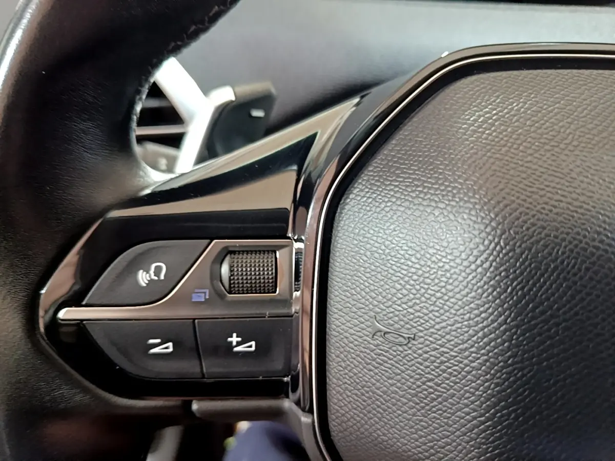 Gros plan sur les commandes gauche du volant cuir du Peugeot 3008 blanc hybride rechargeable, finition Allure 2020.