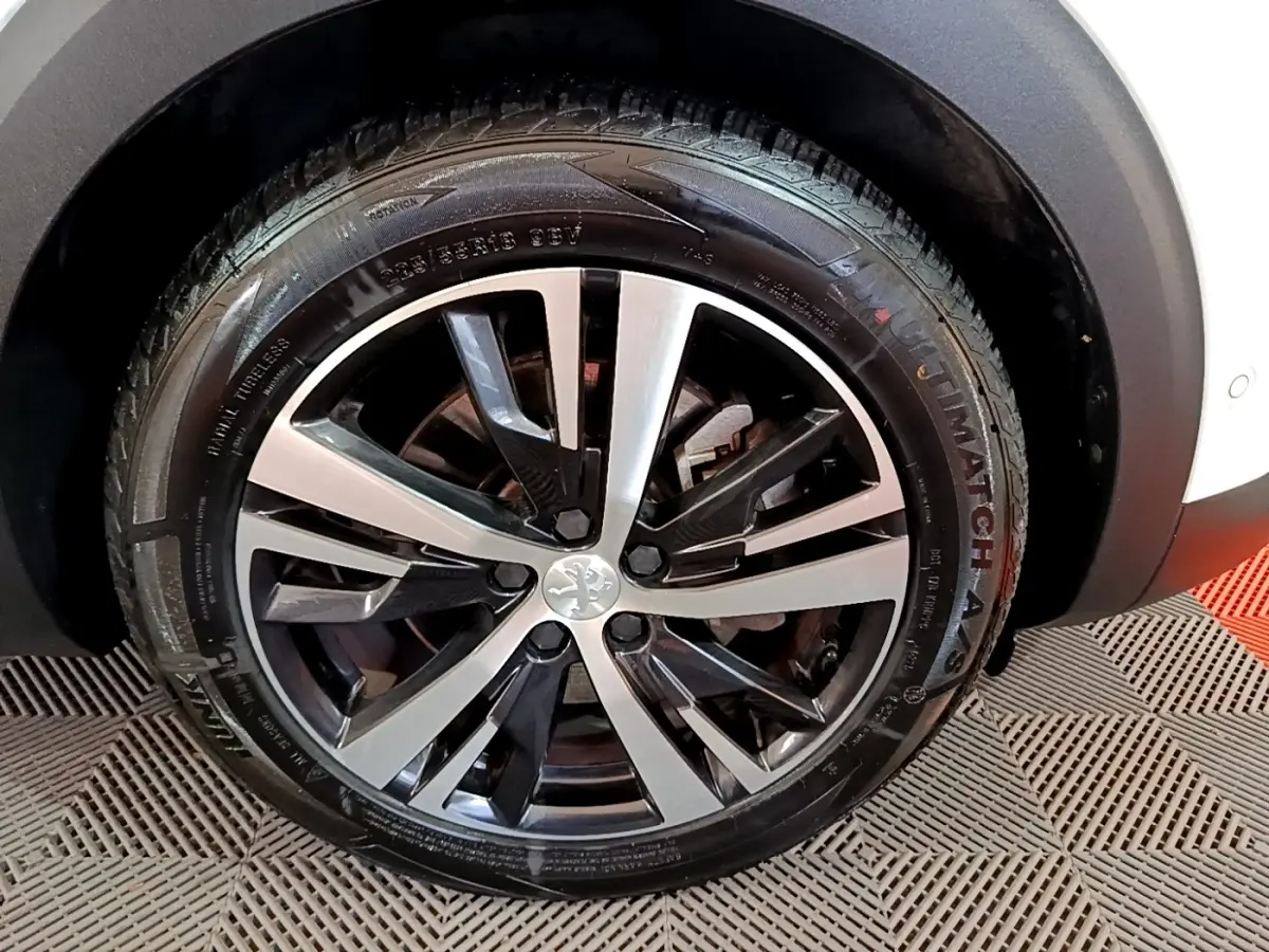 Gros plan sur la roue avant droite du Peugeot 3008 blanc, mettant en valeur la jante alliage bicolore au design moderne.