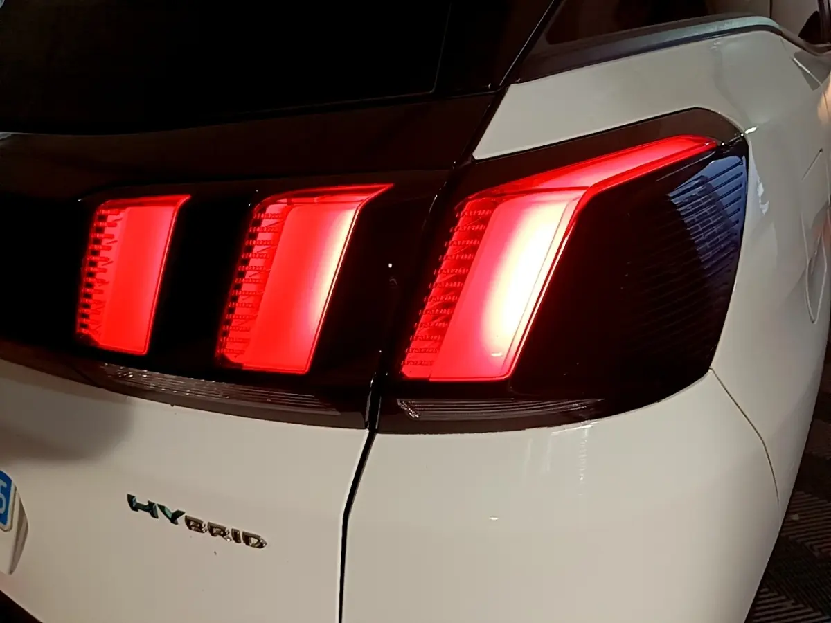 Gros plan sur le feu arrière droit rouge allumé d’un Peugeot 3008 blanc hybride rechargeable, vue arrière.