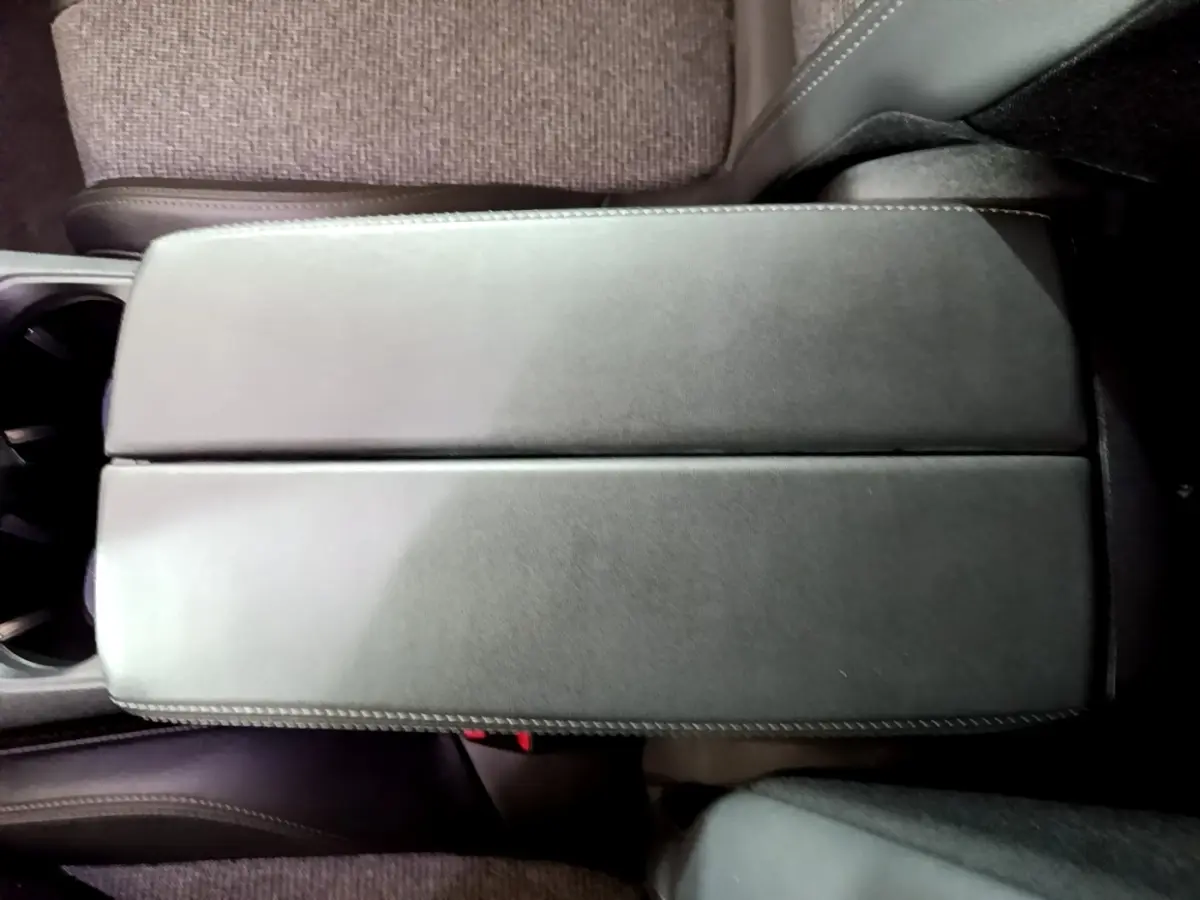 Vue rapprochée de l'accoudoir central en cuir noir à surpiqûres blanches dans l'habitacle du Peugeot 3008 blanc hybride.