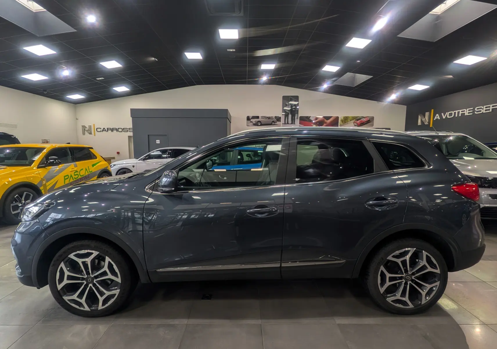 Renault Kadjar TCe 140 Intens gris titanium vu de profil côté gauche dans un showroom lumineux.