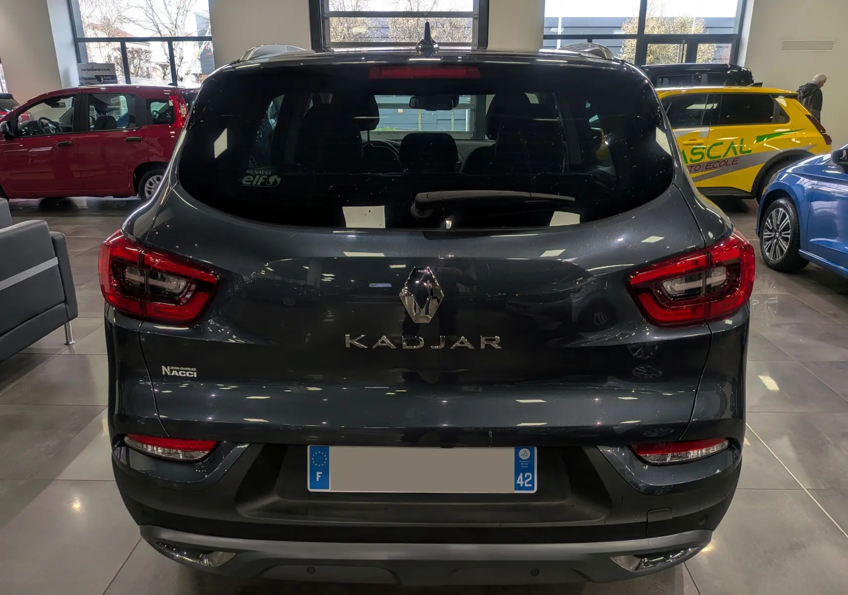 Vue arrière d'un Renault Kadjar gris titanium 2019 dans un showroom, avec feux arrière LED et logo central visible.