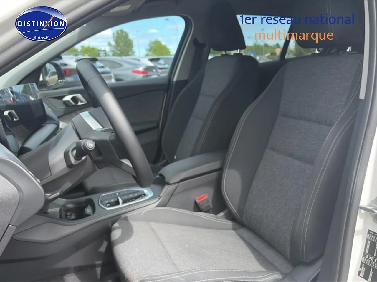 Vue intérieure côté conducteur de la BMW Série 1 blanche, sièges sport gris avec accoudoir central et volant cuir.