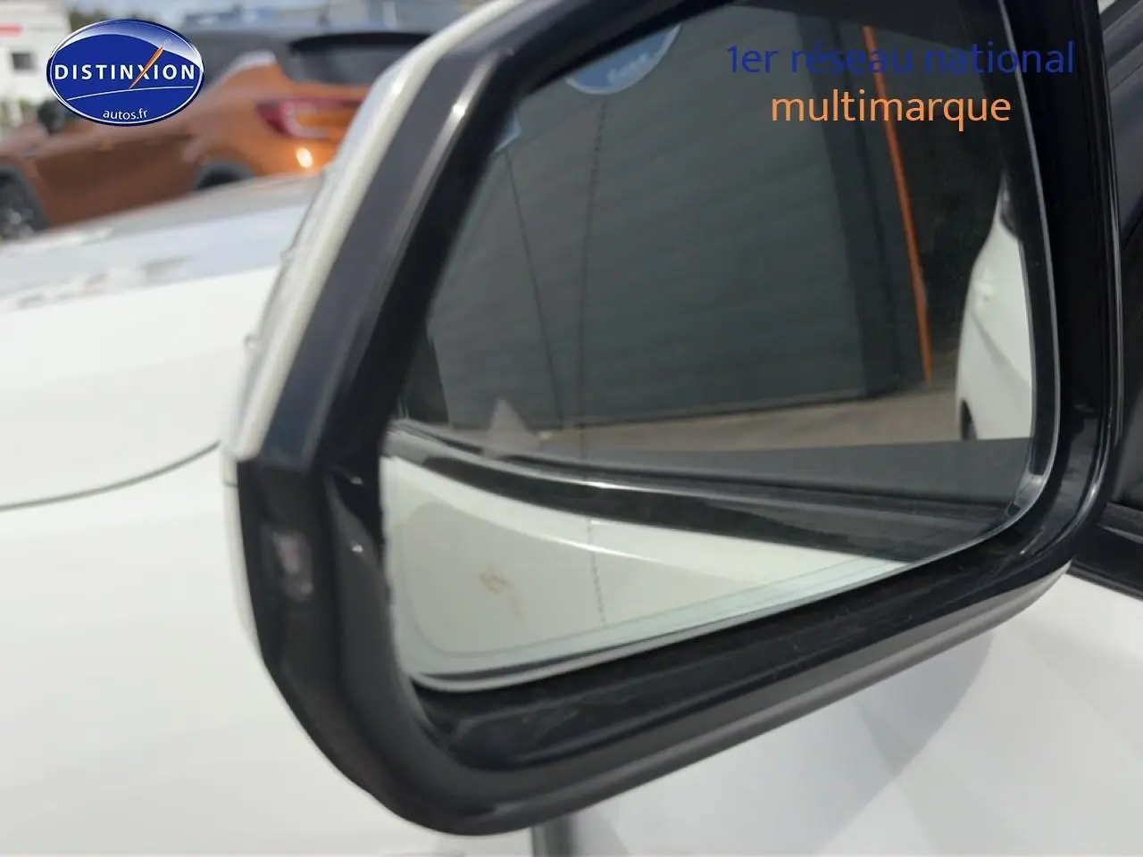 Rétroviseur extérieur côté gauche d'une BMW Série 1 blanche pure, avec reflet du véhicule et arrière-plan flou.