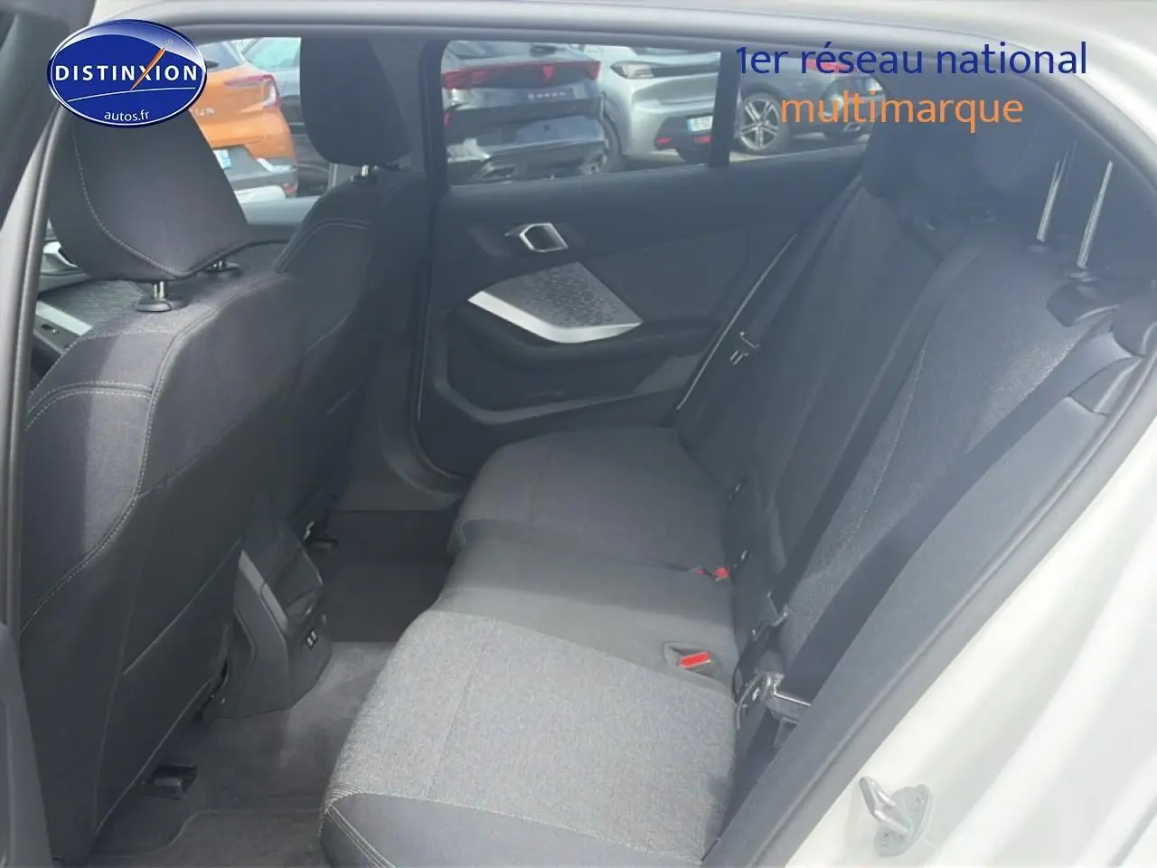 Vue intérieure arrière côté droit de la BMW Série 1 blanche, montrant la banquette tissu et les portes ouvertes.