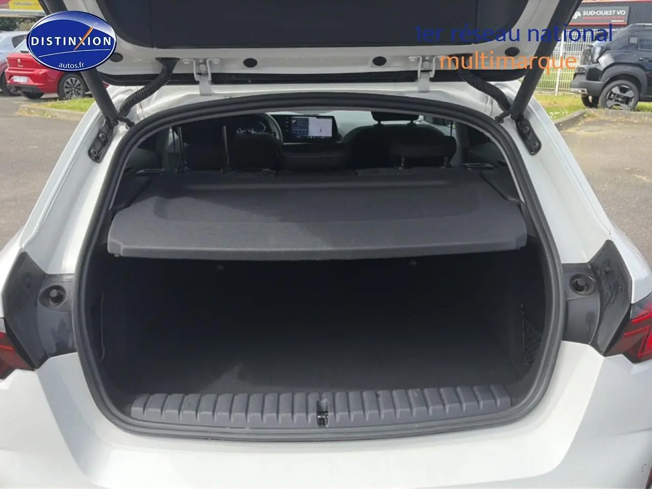 Vue arrière ouverte du coffre d'une BMW Série 1 blanche, montrant l'espace de chargement et la plage arrière.