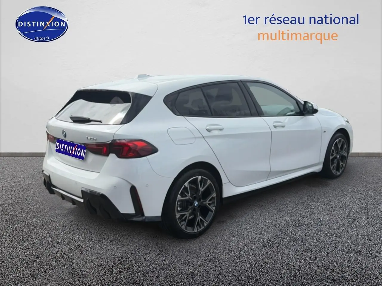 BMW Série 1 blanche vue 3/4 arrière droit, avec jantes alliage noires et feux arrière LED distinctifs.