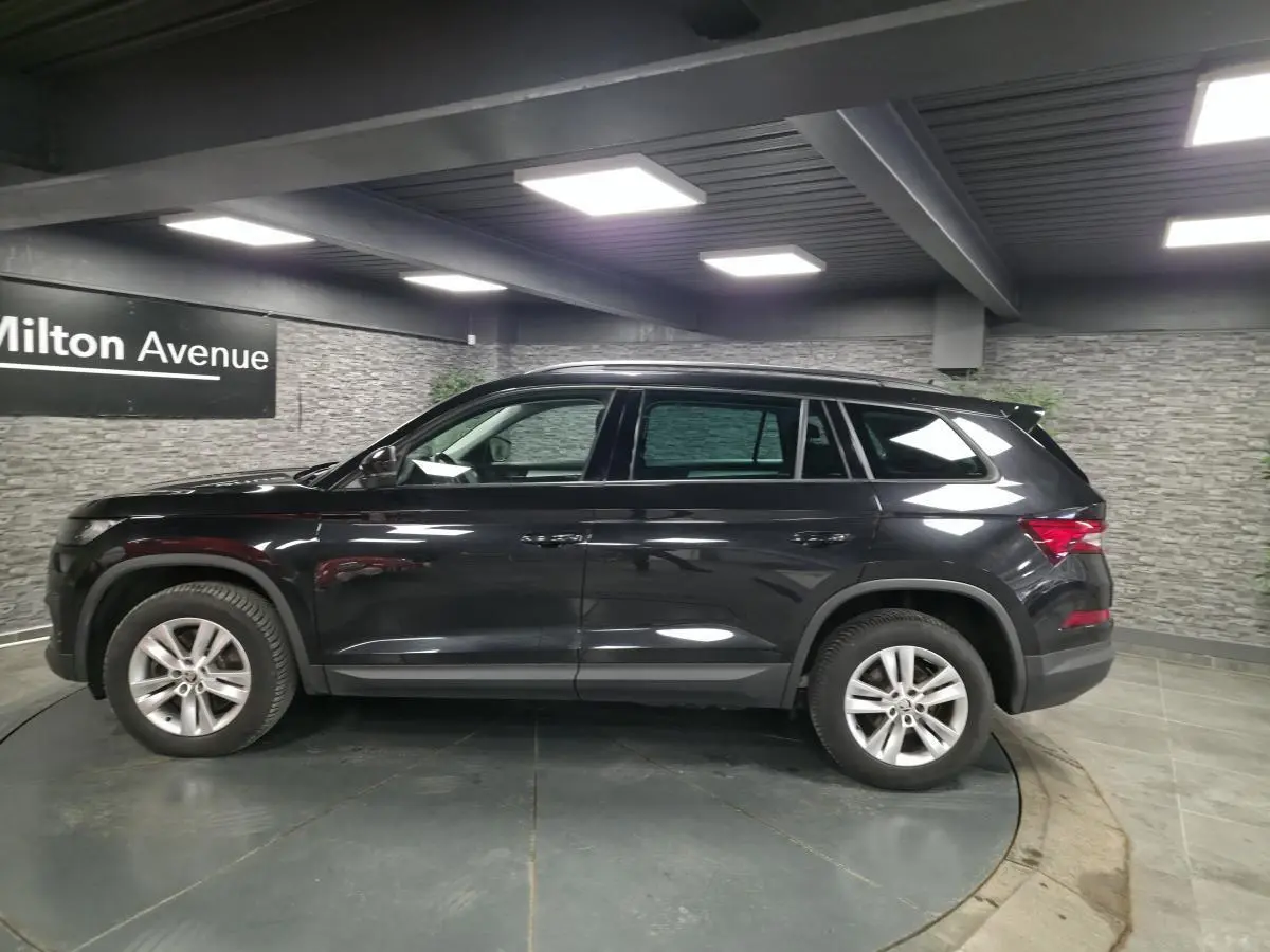 Vue de profil côté gauche d'un SUV Skoda Kodiaq noir métallisé 7 places dans un showroom intérieur.