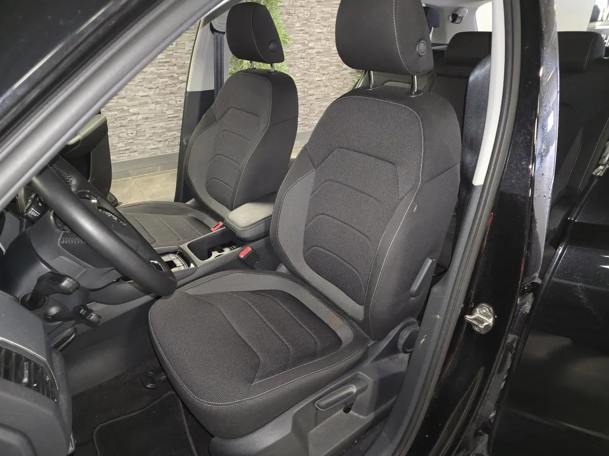 Vue intérieure côté conducteur du Skoda Kodiaq noir 2023, sièges tissu Ambition avec accoudoir central et volant multifonctions.