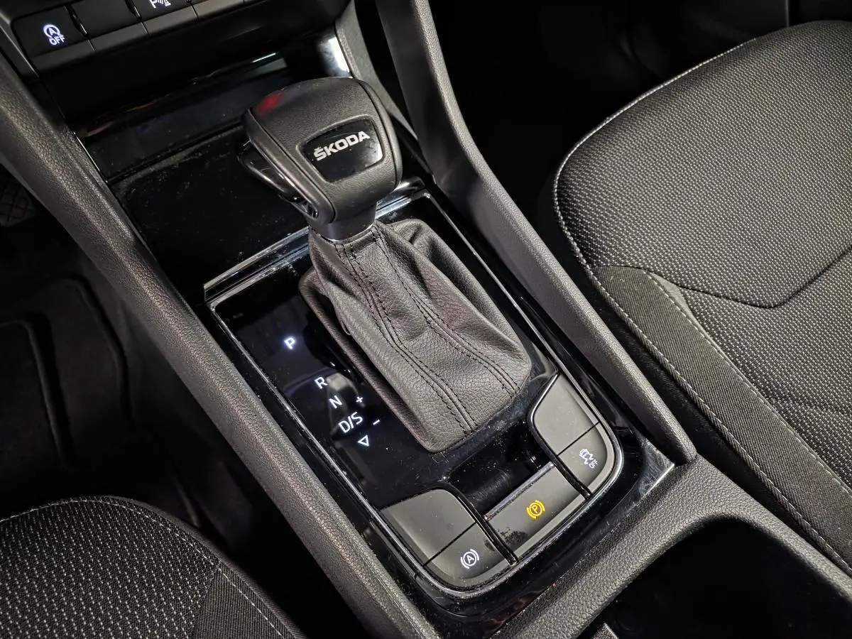 Gros plan sur la console centrale noire du Skoda Kodiaq 2023, avec levier de vitesses automatique et sellerie tissu noire.