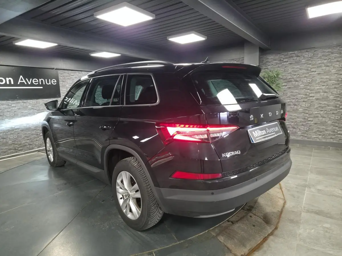 Vue 3/4 arrière droite d'un Skoda Kodiaq noir avec feux arrière allumés dans un showroom.