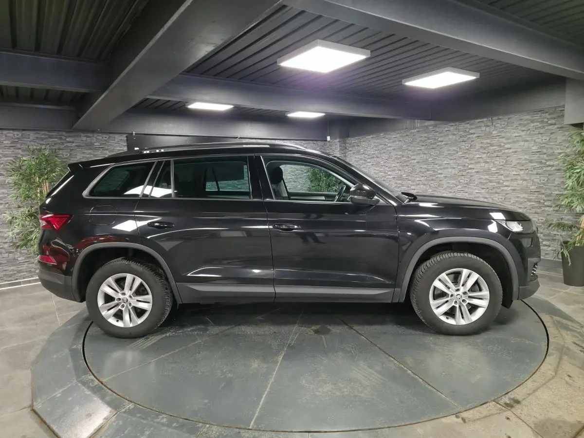 Vue de profil côté gauche d'un SUV Skoda Kodiaq noir métallisé, avec jantes alliage 17 pouces dans un showroom.