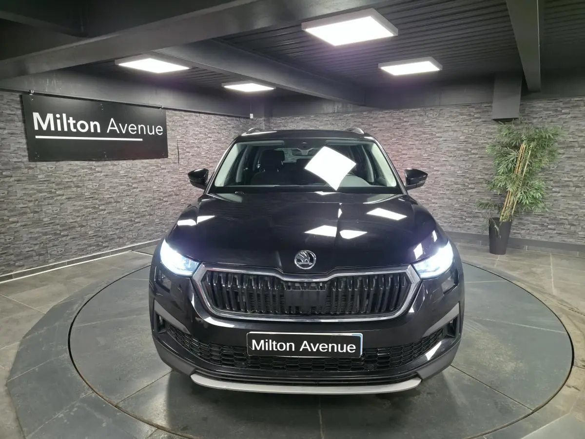 Vue avant d'un Skoda Kodiaq noir 2023 avec phares allumés dans un showroom intérieur.