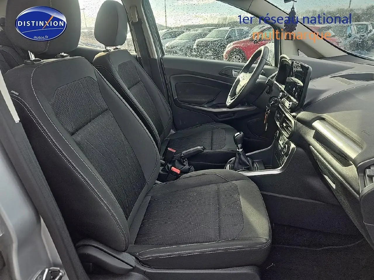 Vue intérieure côté conducteur du Ford EcoSport gris 2019, montrant les sièges en tissu noir et la console centrale avec boîte manuelle.
