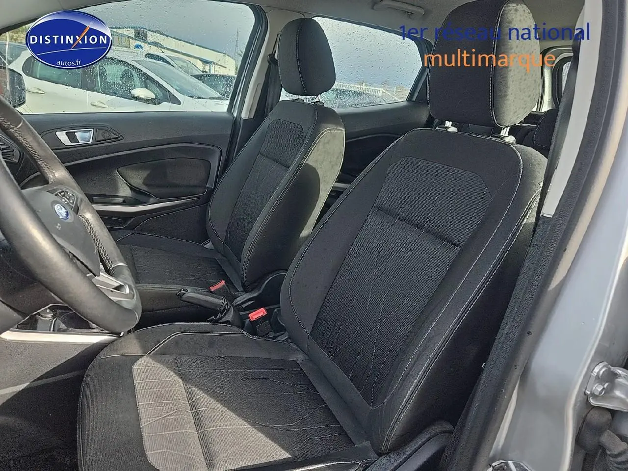 Vue intérieure côté conducteur du Ford EcoSport gris 2019, sièges en tissu noir avec volant cuir multifonction visible.