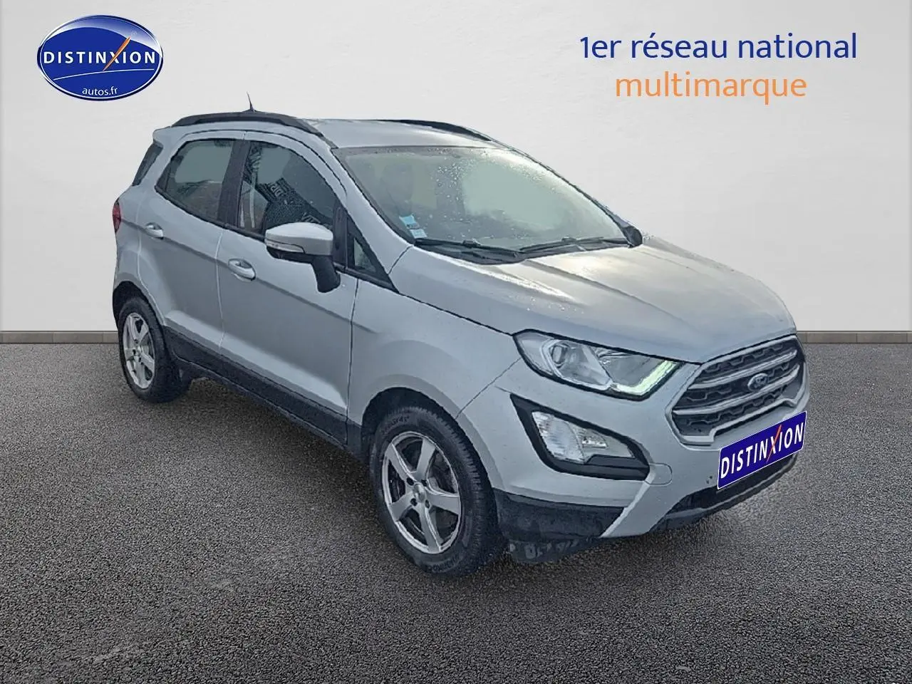 Ford EcoSport gris vue 3/4 avant droit avec jantes alliage et barres de toit visibles sur fond neutre.