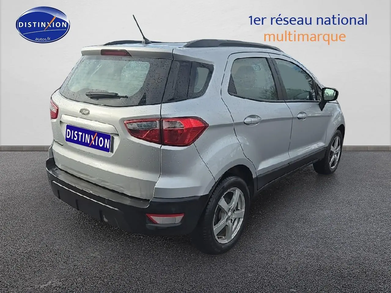 Vue 3/4 arrière droite d'un Ford EcoSport gris 2019 avec jantes alu et barres de toit noires.