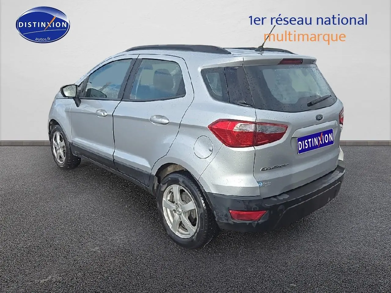Vue 3/4 arrière droite d'un Ford EcoSport gris 2019 avec jantes alu et barres de toit noires.