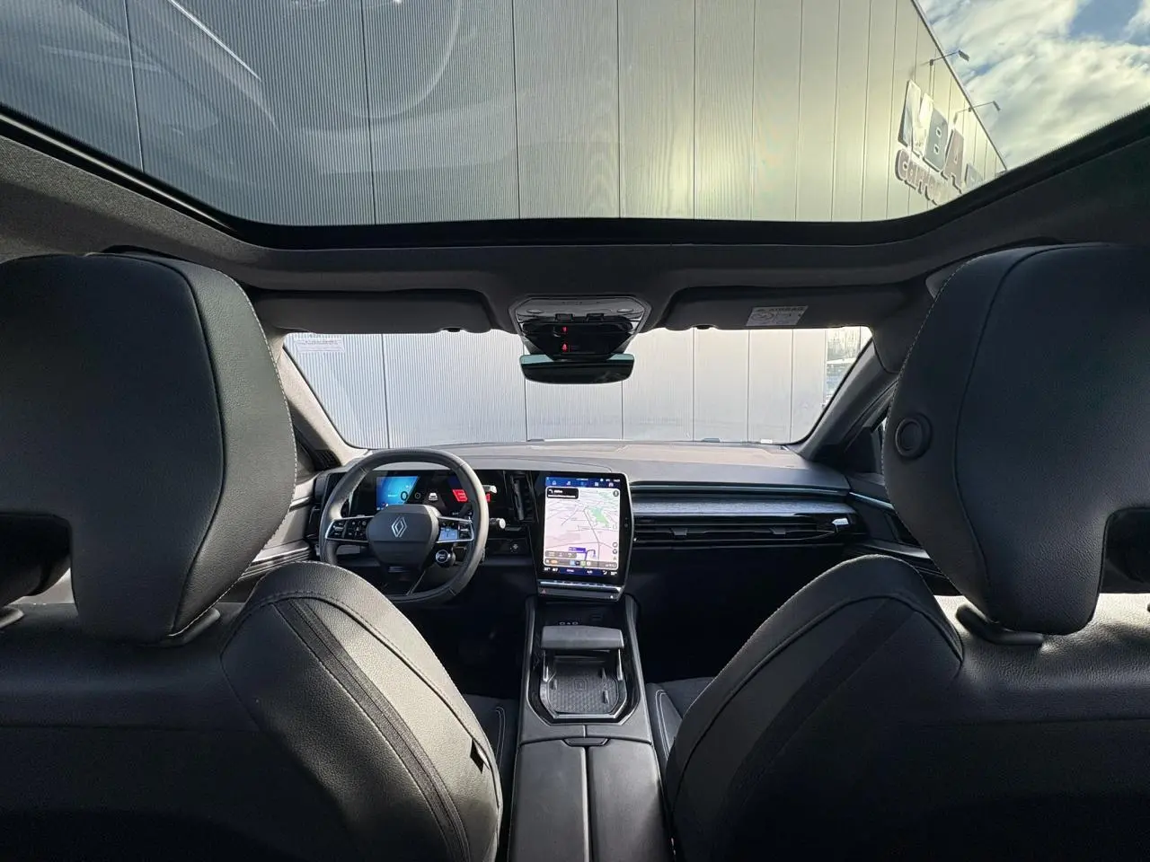 Intérieur Renault Austral E-Tech vu de l'arrière, toit panoramique, tableau de bord avec écran tactile vertical et volant noir.