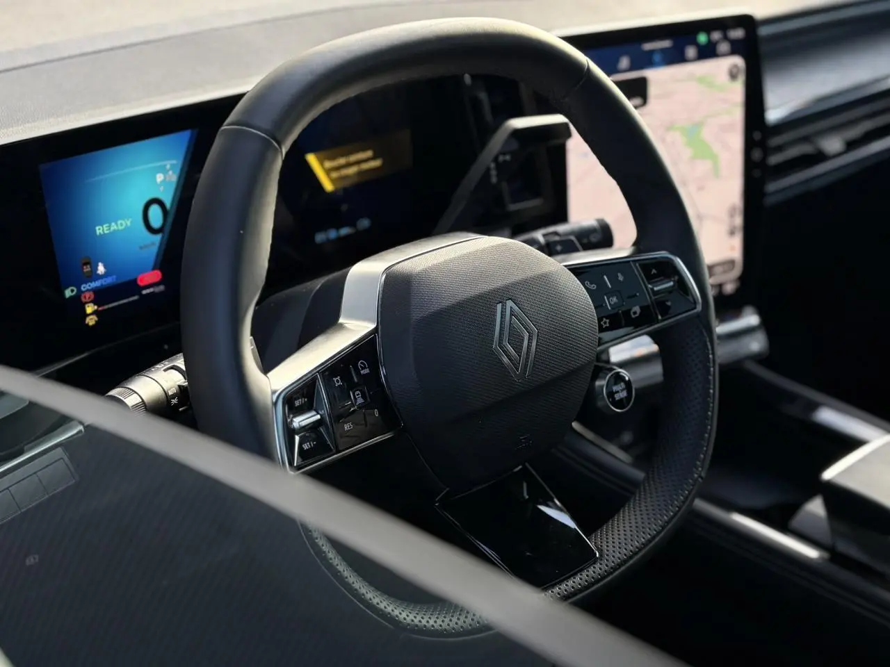 Vue rapprochée du volant noir texturé avec logo Renault, tableau de bord numérique et écran tactile du Renault Austral 2025.