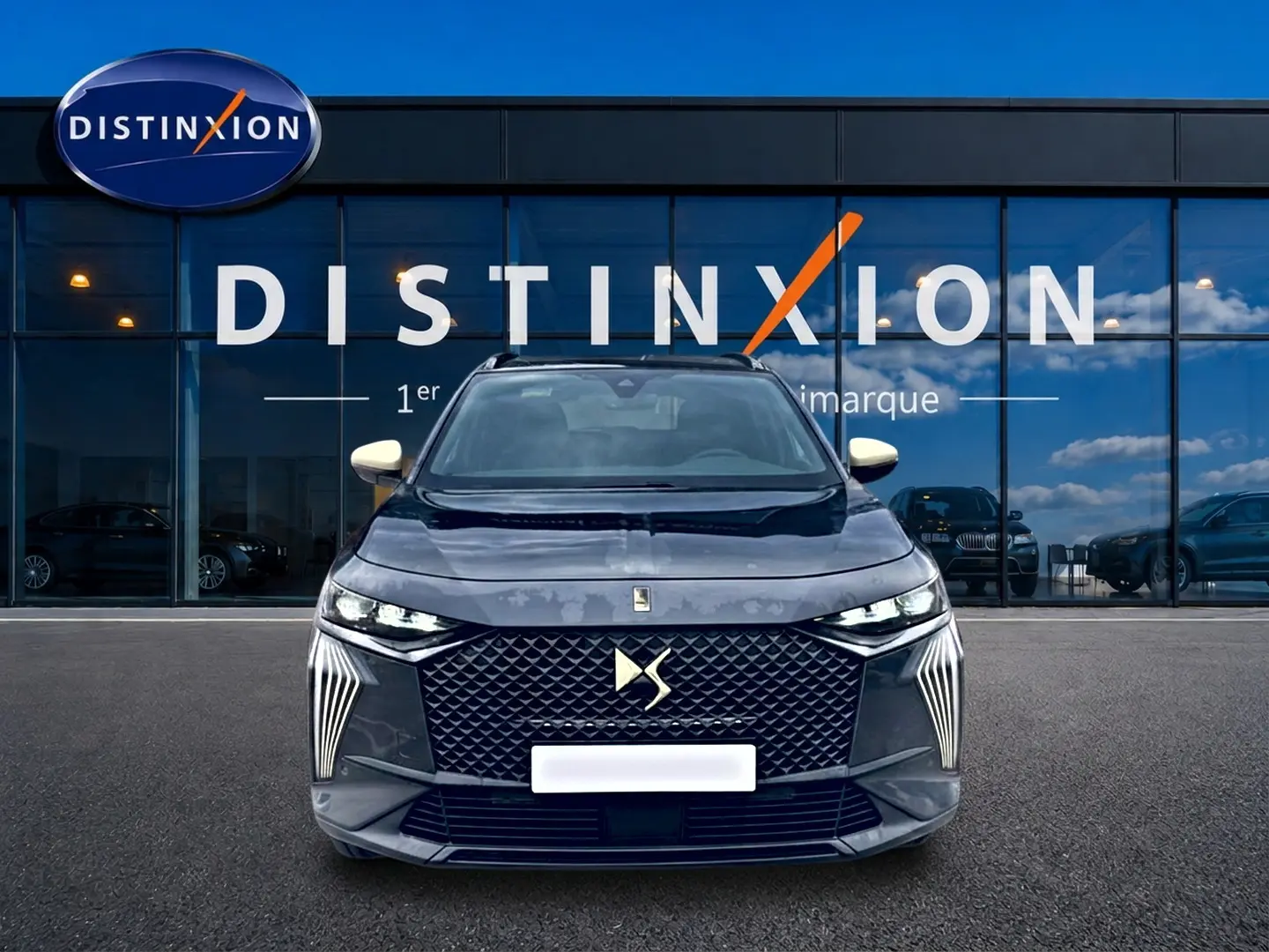 Vue de face du DS7 gris titane 2026 avec calandre distinctive et phares LED fins, devant une vitrine Distinxion.