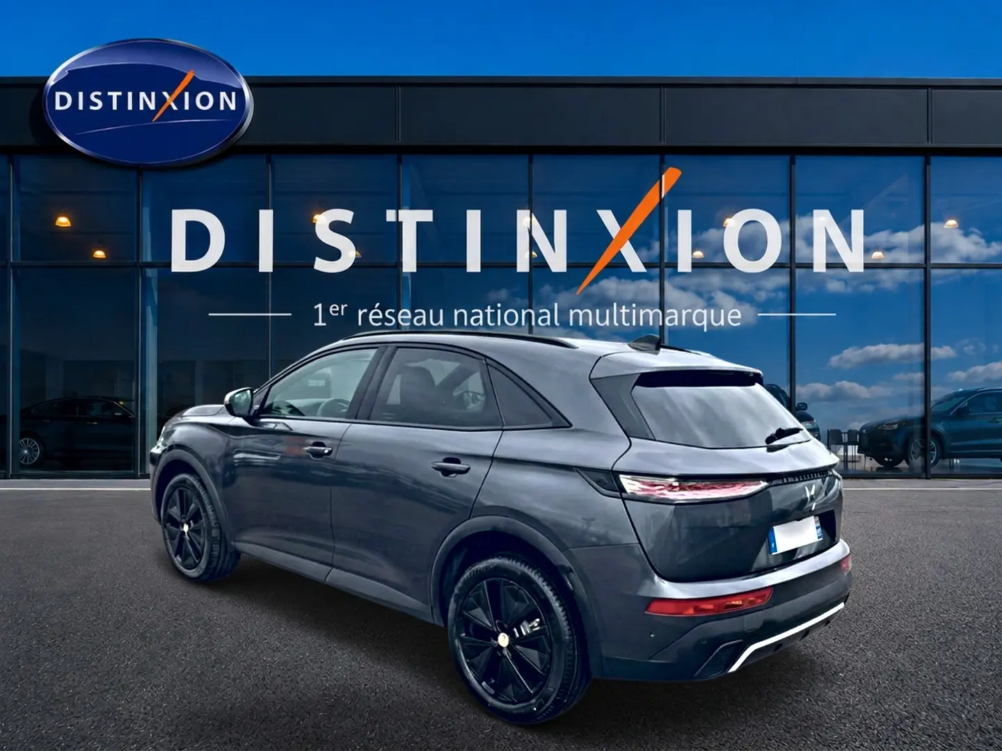 Vue 3/4 arrière droite d'un DS7 gris titane avec jantes noires, garé devant une vitrine Distinxion.