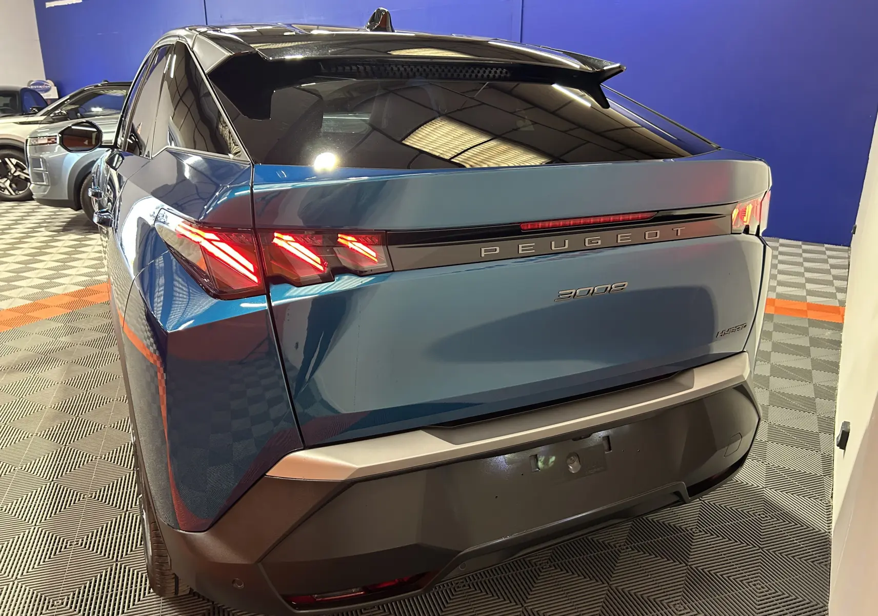 Vue 3/4 arrière droite du Peugeot 3008 III Hybrid bleu obsession avec feux arrière allumés et attelage amovible visible.