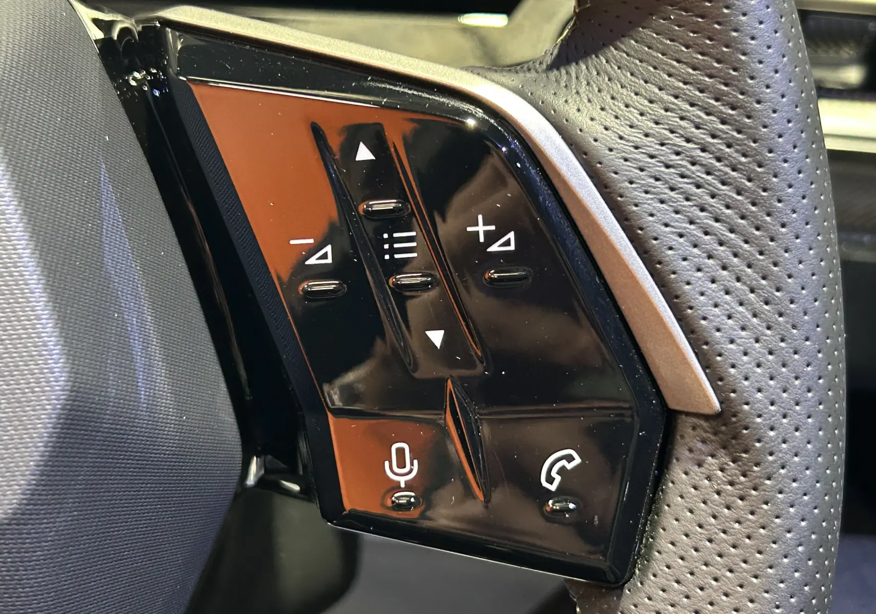 Gros plan sur les commandes noires du volant perforé du Peugeot 3008 III Hybrid 145 e-DCS6 GT, intérieur moderne.