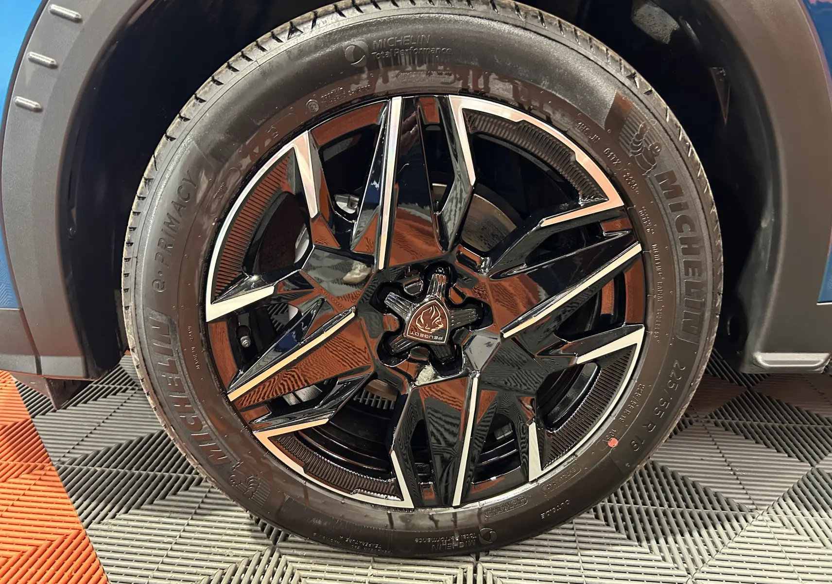 Gros plan sur la roue avant gauche du Peugeot 3008 bleu Obsession, mettant en valeur la jante noire brillante au design géométrique.