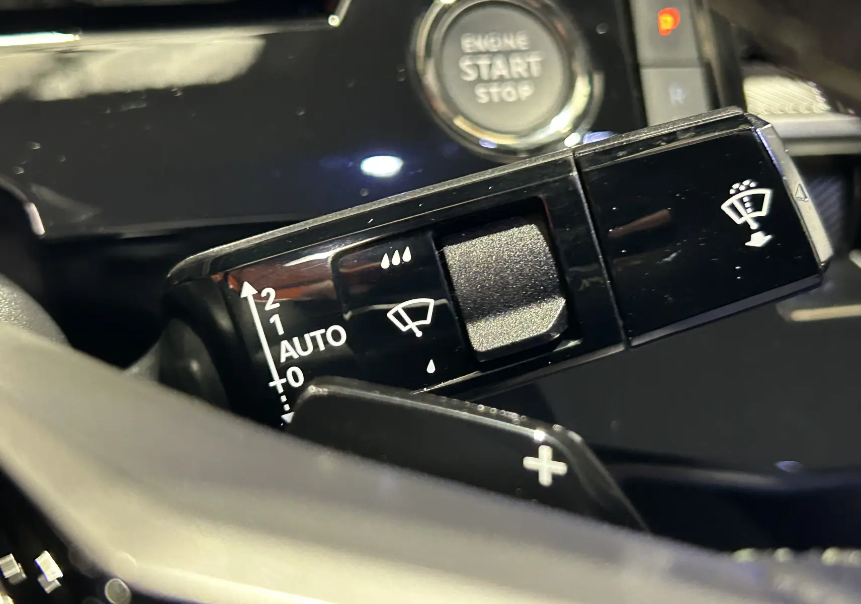 Gros plan sur la commande d’essuie-glace du Peugeot 3008 III Hybrid, avec bouton start/stop en arrière-plan noir brillant.