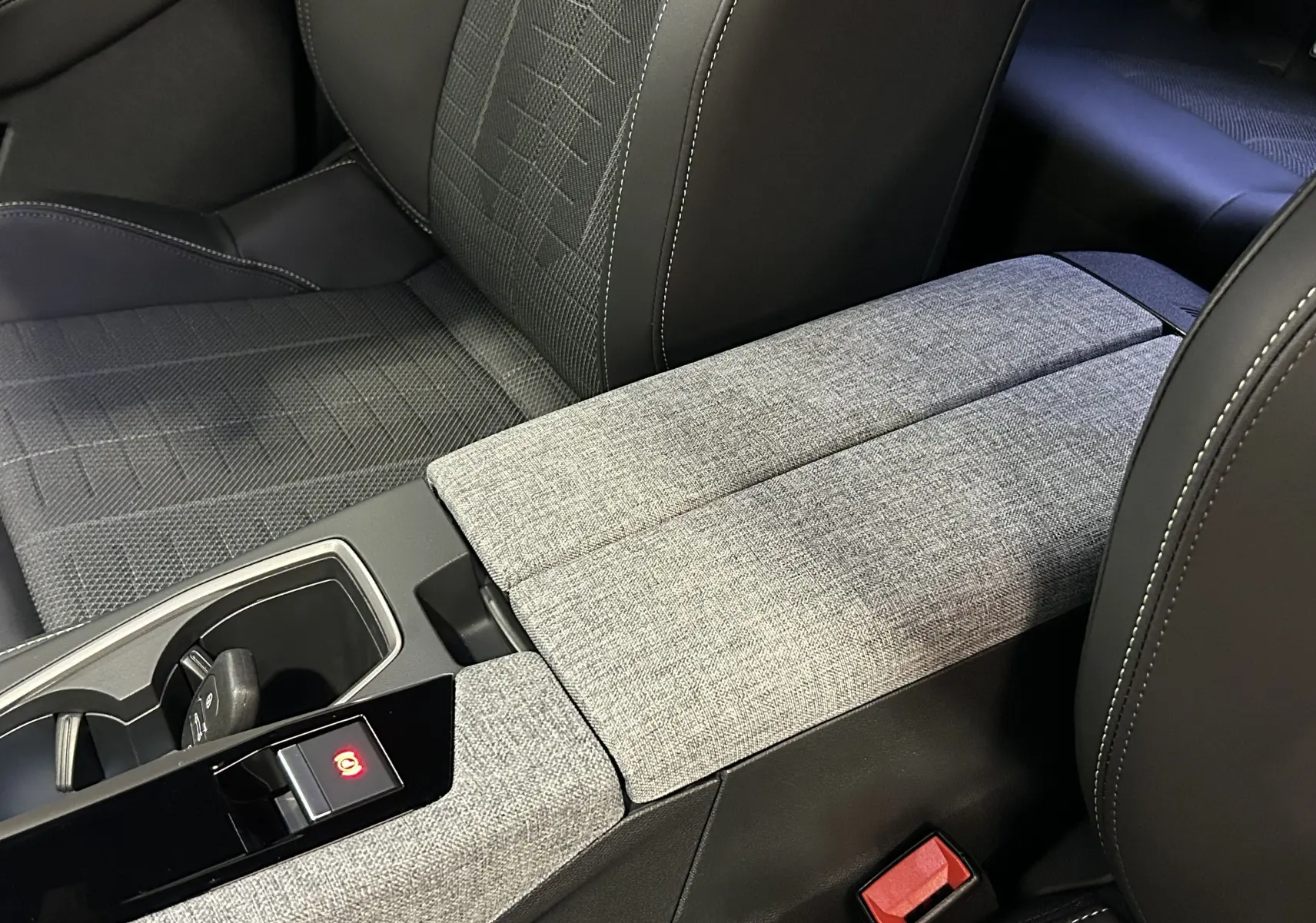 Gros plan sur l'accoudoir central et les sièges avant en tissu gris et cuir noir du Peugeot 3008 III Hybrid 2025.