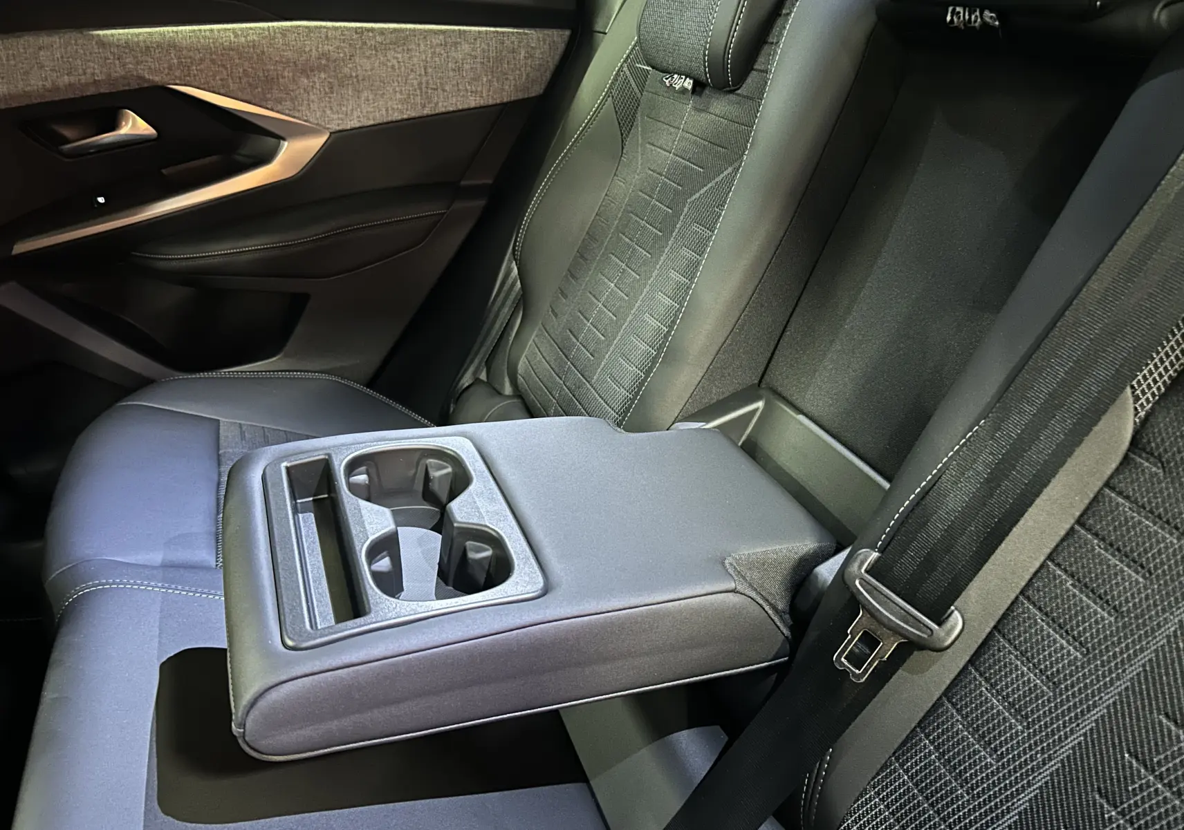 Vue rapprochée de l’accoudoir central arrière avec porte-gobelets du siège arrière du Peugeot 3008 III Hybrid 145 en intérieur noir.