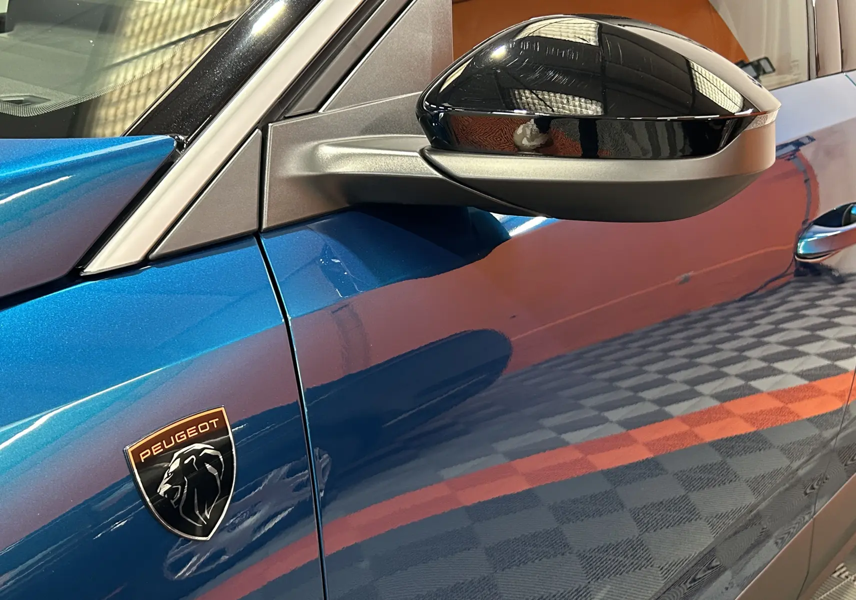 Gros plan sur la porte côté gauche d’un Peugeot 3008 bleu obsession avec rétroviseur noir brillant et logo Peugeot.