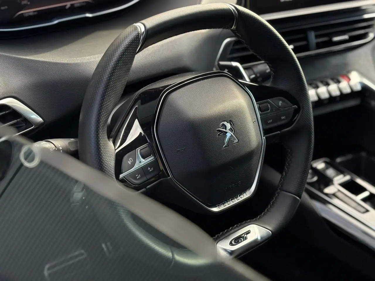Gros plan sur le volant cuir perforé noir avec badge GT du Peugeot 3008 2023, tableau de bord en arrière-plan.