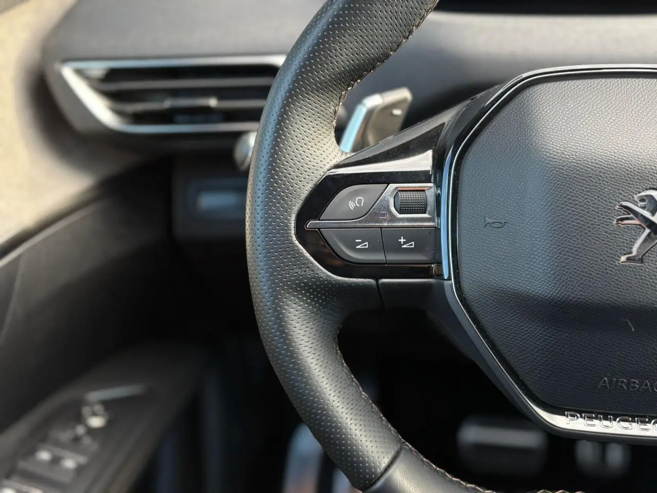 Gros plan sur le volant cuir perforé noir du Peugeot 3008 2023 avec commandes intégrées côté gauche et logo lion chromé.