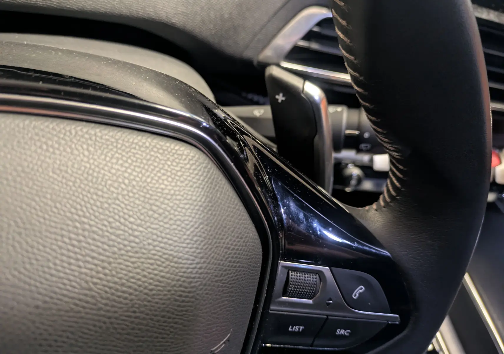 Gros plan sur la partie gauche du volant cuir noir du Peugeot 5008 2024, avec commandes intégrées et palettes au volant.